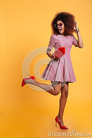 Full length photo of charming african retro stylish woman in dress and high heels standing on one leg while posing with big red l Stock Photo