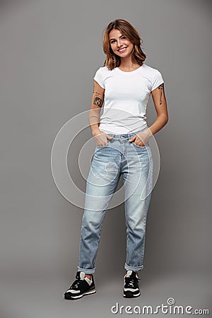 Full length photo of cute brunette woman with hands in her pockets wearing trendy mom jeans and white tshirt, looking at camera Stock Photo