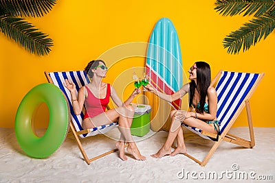 Full length photo of funky sexy girls dressed swimsuits sitting lounge chairs cheering alcohol cocktails isolated yellow Stock Photo