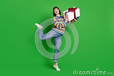 Full length photo of funny carefree young woman wear striped sweater smiling giving gift box isolated green color Stock Photo