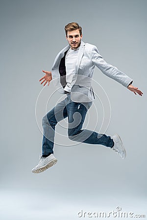 Full-length photo of funny man in casual t-shirt, blazer and jeans running or jumping in air isolated over gray Stock Photo