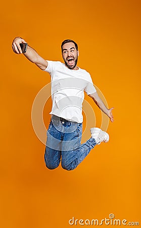Full length photo of optimistic guy 30s in casual wear laughing and taking selfie on cell phone, isolated over yellow background Stock Photo