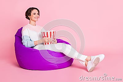Full length photo portrait of woman with big popcorn bag sitting in violet beanbag chair isolated on pastel pink colored Stock Photo
