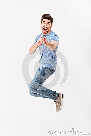 Full-length photo of positive man in casual t-shirt and jeans jumping and pointing finger on camera, isolated over white Stock Photo