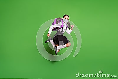 Full length photo of schoolgirl pigtails running jumping wear mask backpack isolated on vivid green colored background Stock Photo
