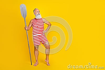 Full length photo of senior bearded masculine pensioner holding wooden boat oars looking empty space isolated on yellow Stock Photo