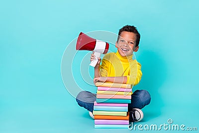 Full length photo of small cheerful boy sitting floor pile stack book hand hold loudspeaker isolated on cyan color Stock Photo