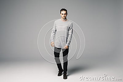 Full length photo of a young fashion man with his hands folded, looking into the camera and smiling.on gray background Stock Photo