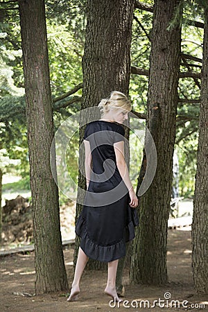 Full length portrait of beautiful barefooted young women wearing black dress while standing under pine tree Stock Photo