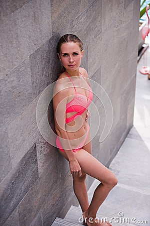 Full-length portrait of beautiful girl in the pink swimsuit with shapely body is posing near the swimming pool on Stock Photo