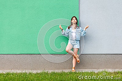 Full length portrait of beautiful woman in casual jeans denim style in summertime standing near green and light blue wall and Stock Photo
