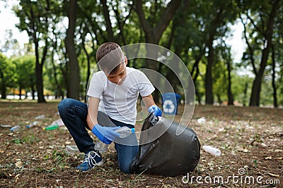 A little child picking up the garbage and putting it in a black garbage bag on a natural background. Ecology protection Stock Photo