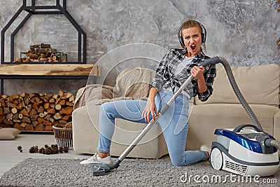 Full length portrait of cheerful young woman 20s listening to music via headphones and having fun with vacuum cleaner in Stock Photo