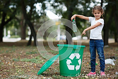 A little child putting the garbage in a green recycling bin on a blurred natural background. Ecology pollution concept. Stock Photo