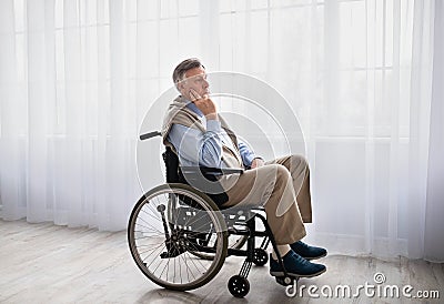 Full length portrait of handicapped senior man in wheelchair feeling desperate and lonely, looking out window indoors Stock Photo