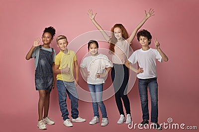 Full length portrait of happy diverse schoolkids making different gestures on pink background Stock Photo