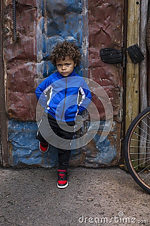 Full length portrait of an mixed race little boy standing on a dirty city street Stock Photo