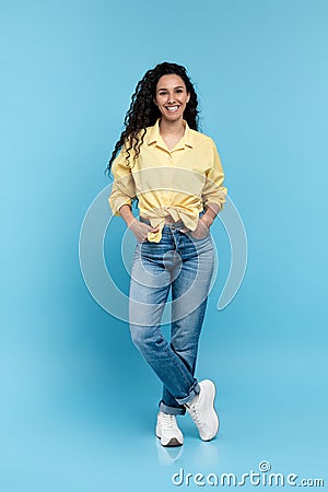 Full length portrait of positive young woman in trendy casual outfit standing and looking at camera over blue background Stock Photo