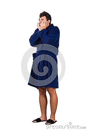 Full length portrait of scared and worried young man messy hair, wears blue bathrobe, waking up after dreamt a nightmare, bites Stock Photo