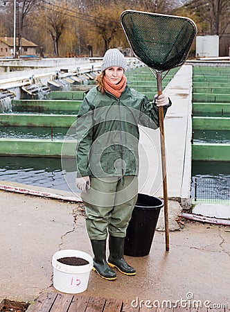 Full-length portrait of female with landing net on fish farm Stock Photo