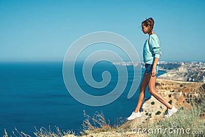Full length portrait of young slim woman taking step above the cliff, standing in front beautiful sea view. Stock Photo