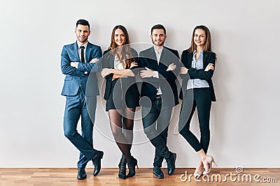 Full length portrait of young and smiling business people with arms crossed lean to wall in office Stock Photo