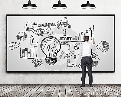 Full length rear view of businessman in formal clothes who is drawing a business flowchart on the whiteboard. Concrete wall, woode Stock Photo