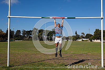 Full length of rugby player hanging on goal post at field Stock Photo