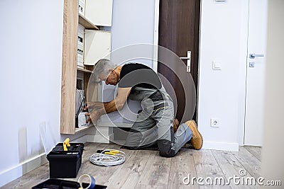 Full length shot of aged electrician, repairman in uniform working, installing an ethernet cable for router in fuse box Stock Photo