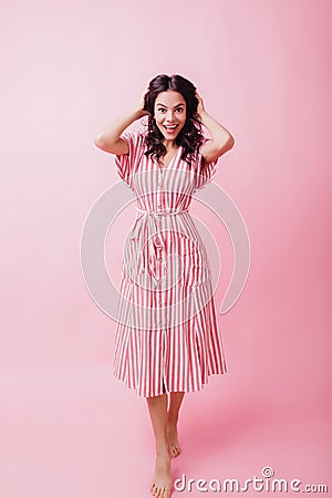 Full-length shot of barefooted girl in long dress laughing to camera. Indoor photo of amazing brune Stock Photo
