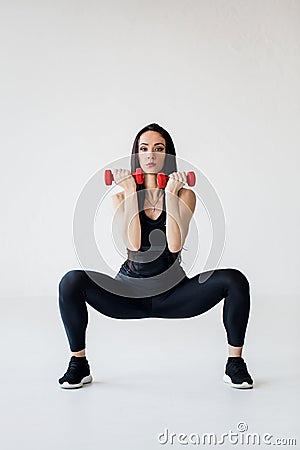Full-length shot of the cardio tutorials. The athletic trainer is doing squat tricep extension with red dumbbells at the Stock Photo