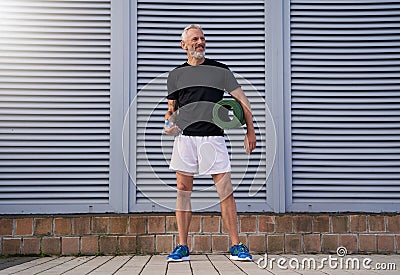 Full length shot of middle aged sportsman doing sport outdoors, standing with exercise mat and a bottle of water Stock Photo