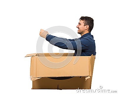 Full length side view of childish man sitting inside a cardboard box pretending to drive a new car isolated over white background Stock Photo