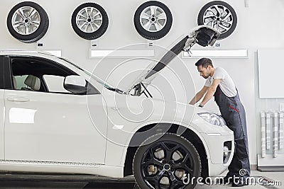 Full length side view of male mechanic examining car engine in repair shop Stock Photo