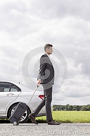 Full length side view of young businessman with luggage walking by broken down car at countryside Stock Photo