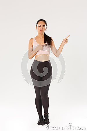 Full length of skeptical, disappointed asian fitness girl, sportswoman smirk and sulking while complaining on bad gym or Stock Photo