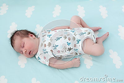 Full length of sleeping Caucasian baby one month old, lying on light blue bedsheet with white clouds Stock Photo