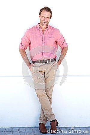 Full length smiling older man leaning against white wall Stock Photo