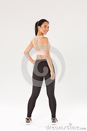 Full length of smiling slim and strong female fitness coach, female athelte in sportswear turn behind to look at camera Stock Photo
