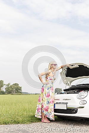 Full-length of tensed woman standing by broken down car on country road Stock Photo