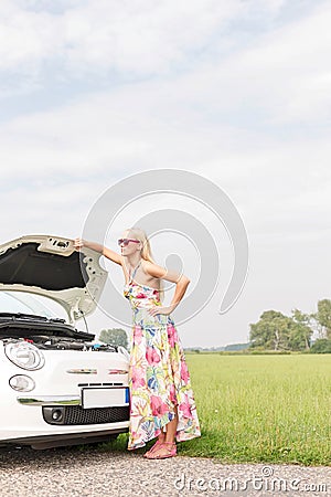 Full-length of tensed woman standing by broken down car on country road Stock Photo