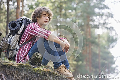 Full length of thoughtful male backpacker relaxing on cliff in forest Stock Photo