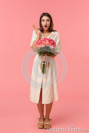 Full-length vertical portrait pretty surprised girl receive unexpected gift, got delivery holding flowers, gasping open Stock Photo