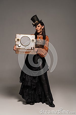 Length view of woman in top hat with goggles showing steampunk laptop on grey Stock Photo