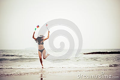 Full Length Of Woman Holding Pinwheel Toys While Jumping At Beach Stock Photo