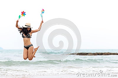 Full Length Of Woman Holding Pinwheel Toys While Jumping At Beach Stock Photo