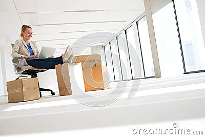 Full length of young businesswoman using laptop with feet up on moving box in office Stock Photo