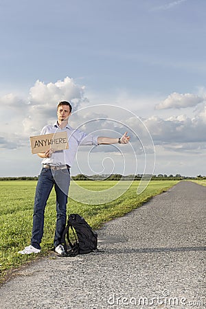 Full length of young man hitching while holding anywhere sign on countryside Stock Photo