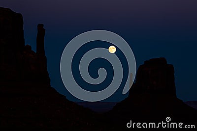 Full moon in dark sky above silhouette of desert towers in Souther Utah/Arizona Monument Valley Stock Photo