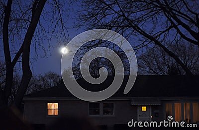 Moon rise over a house with lights on. Stock Photo